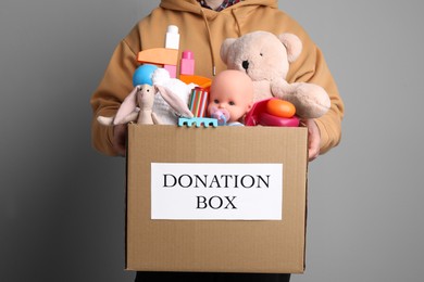 Photo of Man holding donation box full of different toys on grey background, closeup