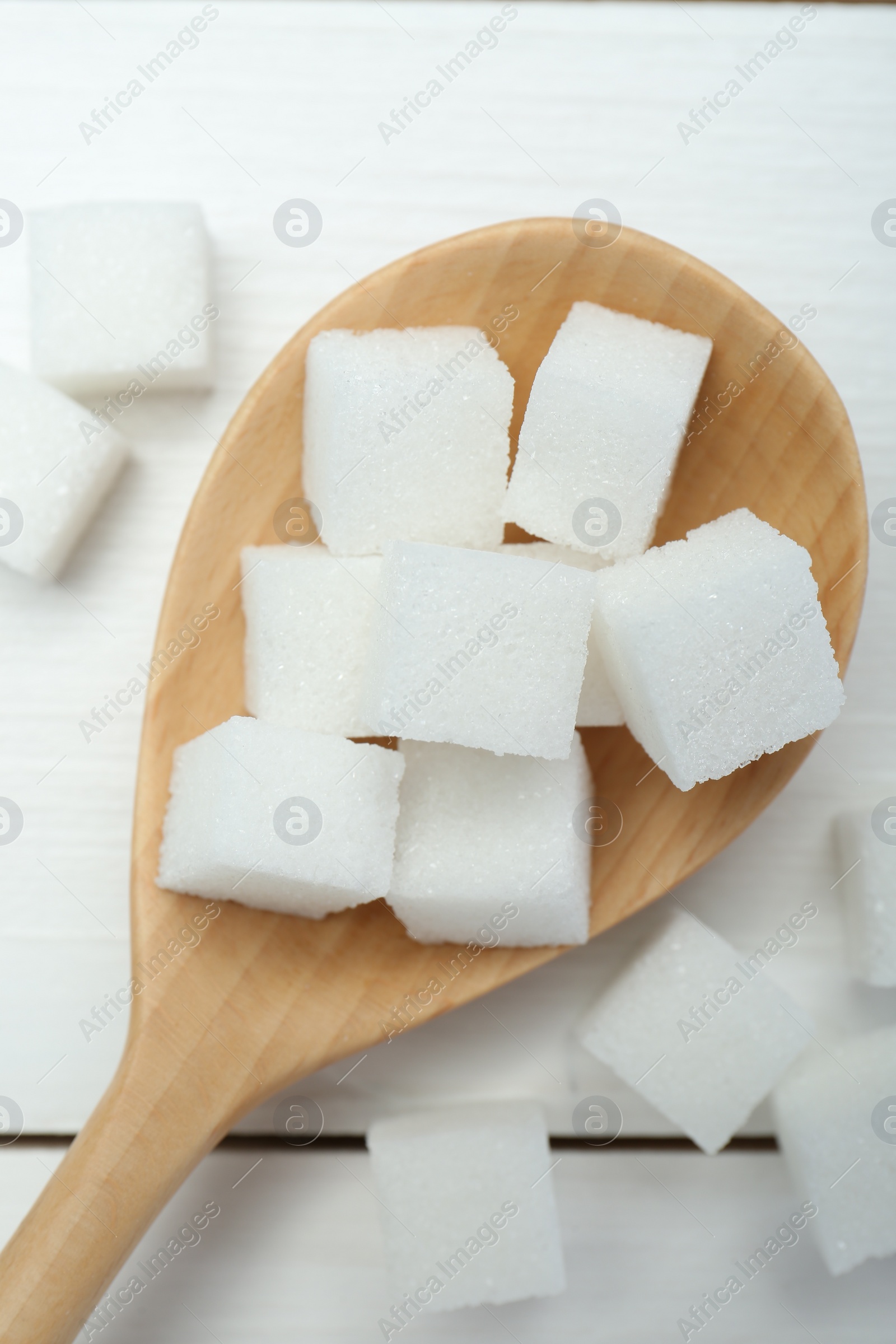 Photo of Many sugar cubes and wooden spoon on white table, top view