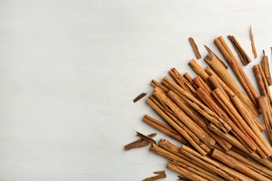 Photo of Aromatic cinnamon sticks on white wooden table, flat lay. Space for text