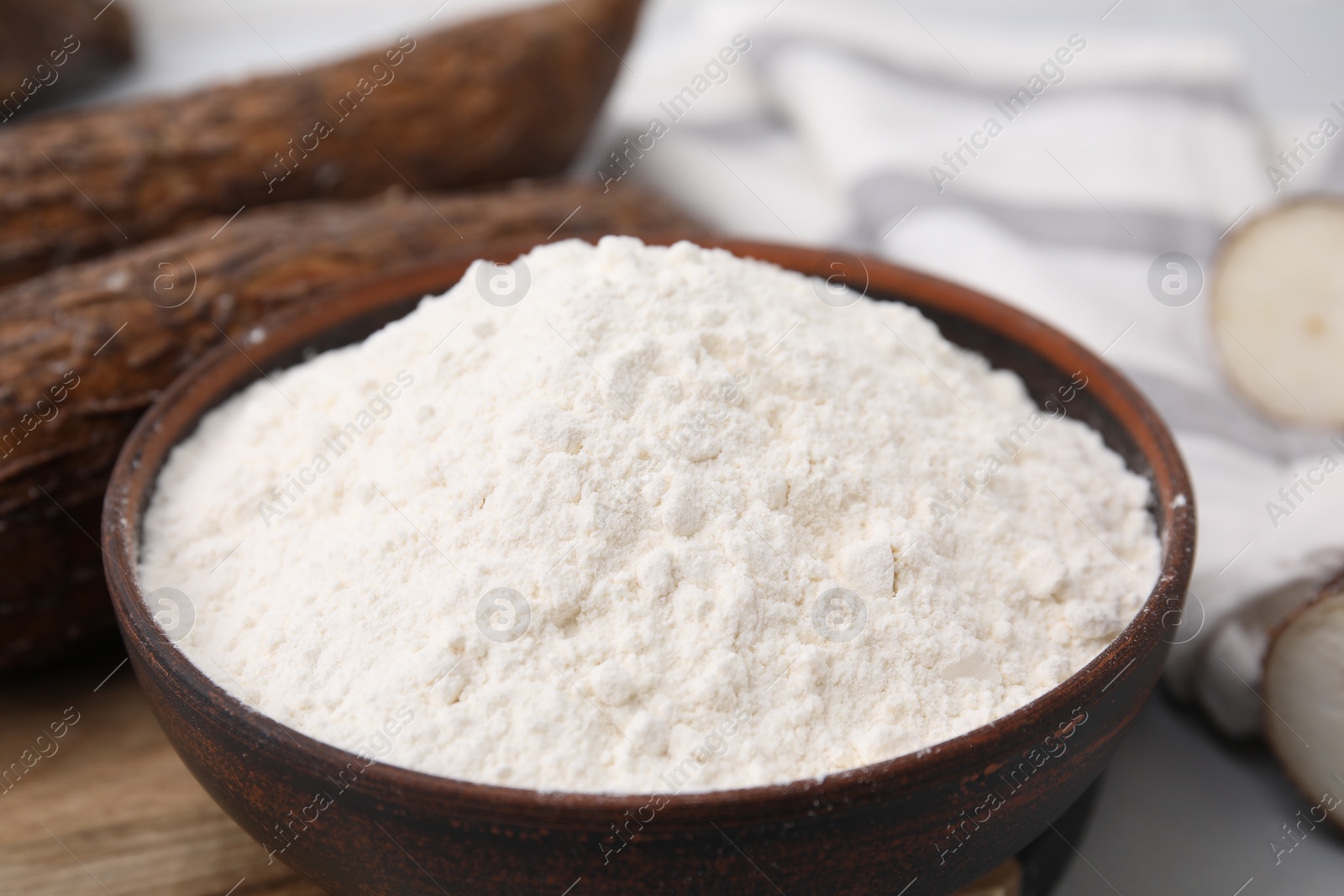 Photo of Bowl with cassava flour and roots on table, closeup