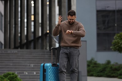 Photo of Being late. Worried man with suitcase looking at watch outdoors, space for text