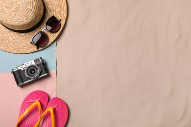 Photo of Beach towel, hat, sunglasses, camera and flip flops on sand, flat lay. Space for text