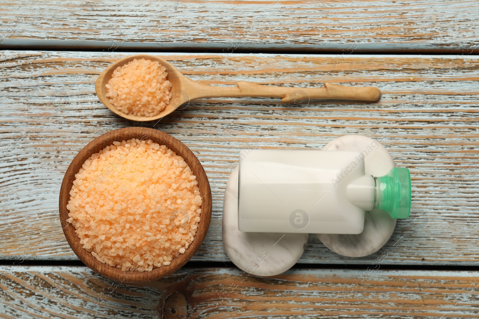 Photo of Orange sea salt in bowl, spa stones, cosmetic product and spoon on wooden table, flat lay