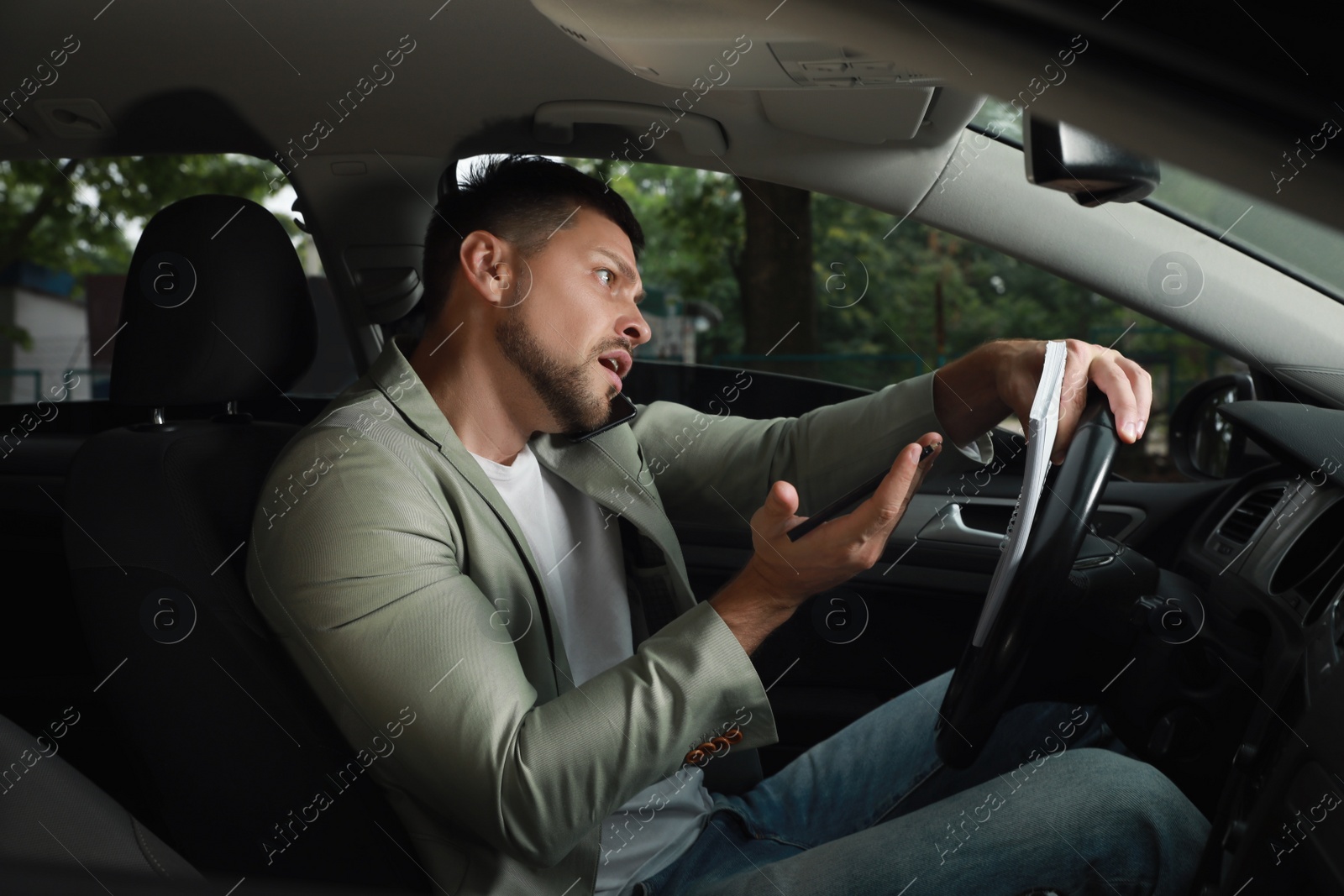 Photo of Stressed businessman talking on phone in driver's seat of modern car