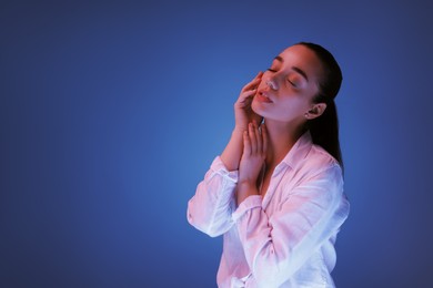 Portrait of beautiful young woman posing on blue background with neon lights, space for text