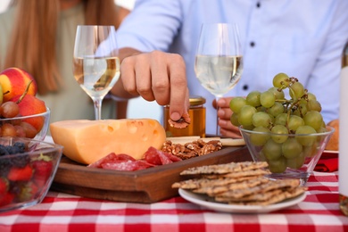 Photo of Young man tasting snacks at picnic table, closeup