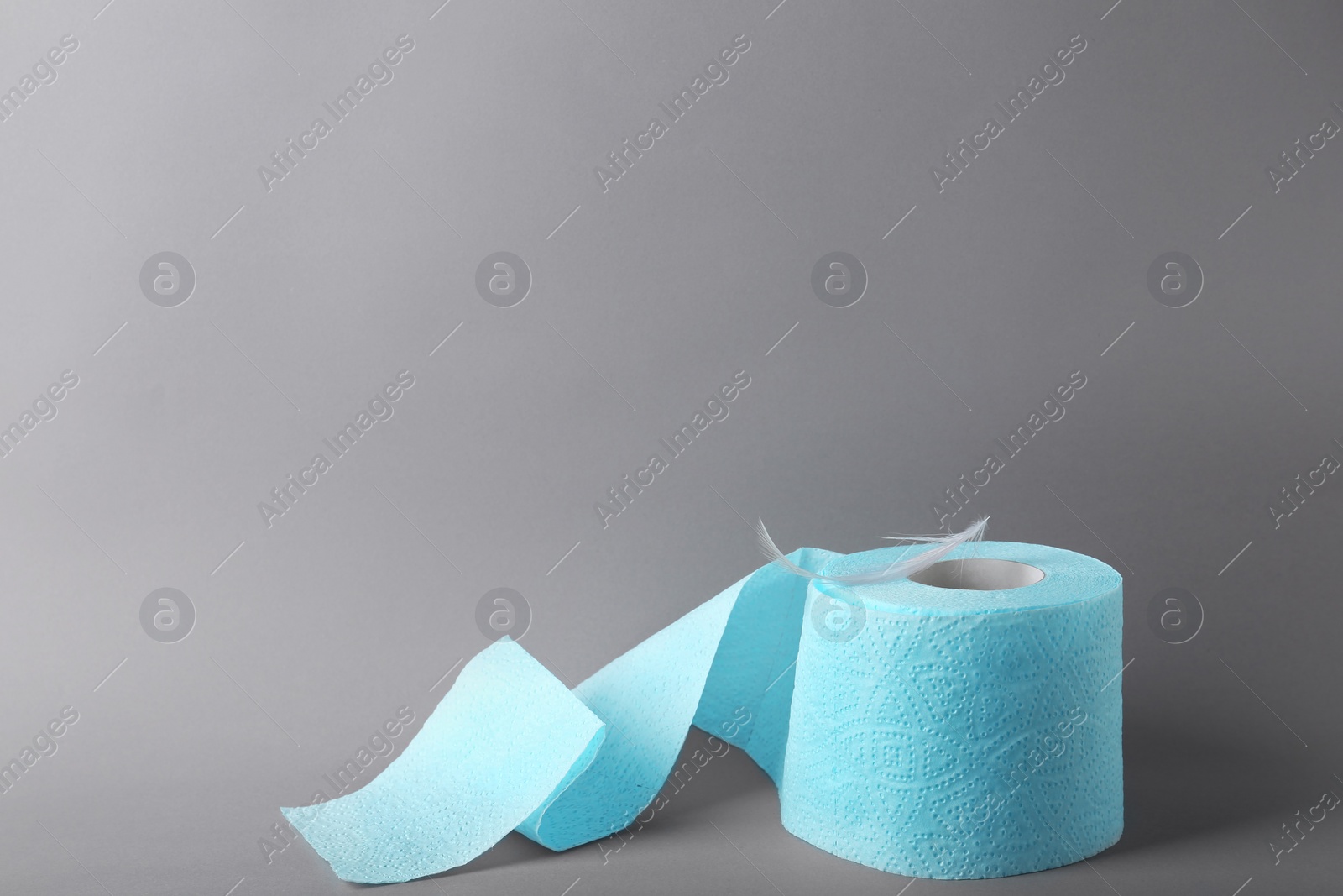 Photo of Roll of toilet paper with feather on grey background. Space for text