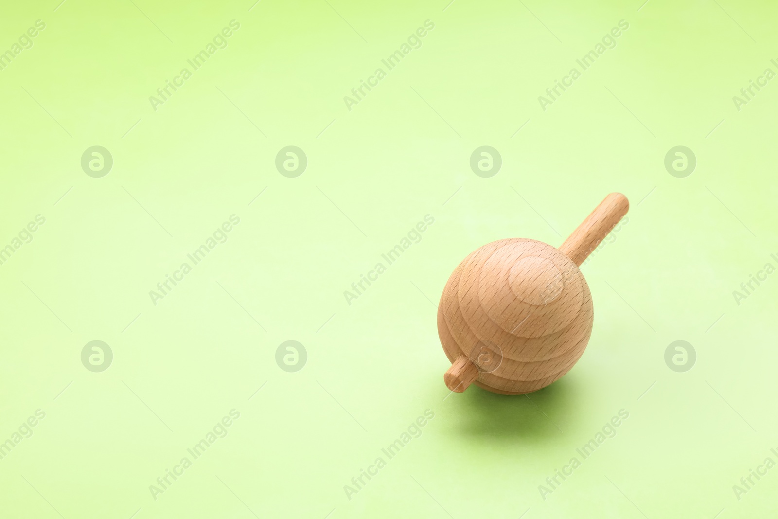 Photo of One wooden spinning top on light green background, space for text. Toy whirligig