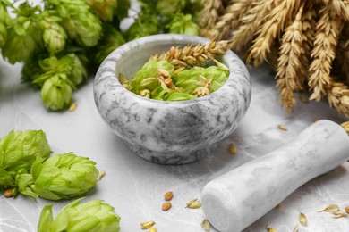 Photo of Mortar with pestle, fresh hops and ears of wheat on light grey marble table, closeup