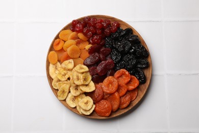 Delicious dried fruits on white tiled table, top view