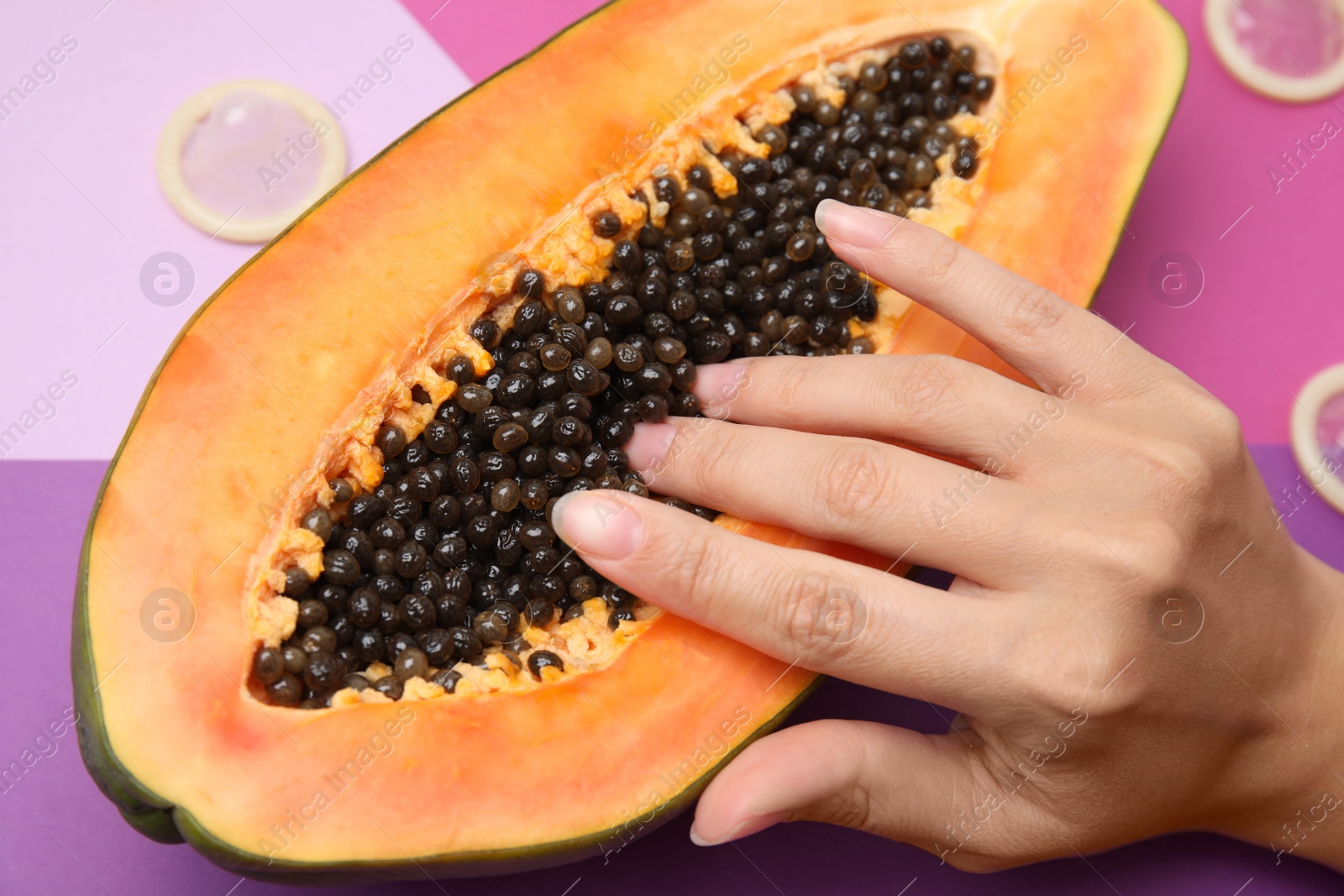 Photo of Young woman touching half of papaya and condoms on color background, closeup. Sex concept