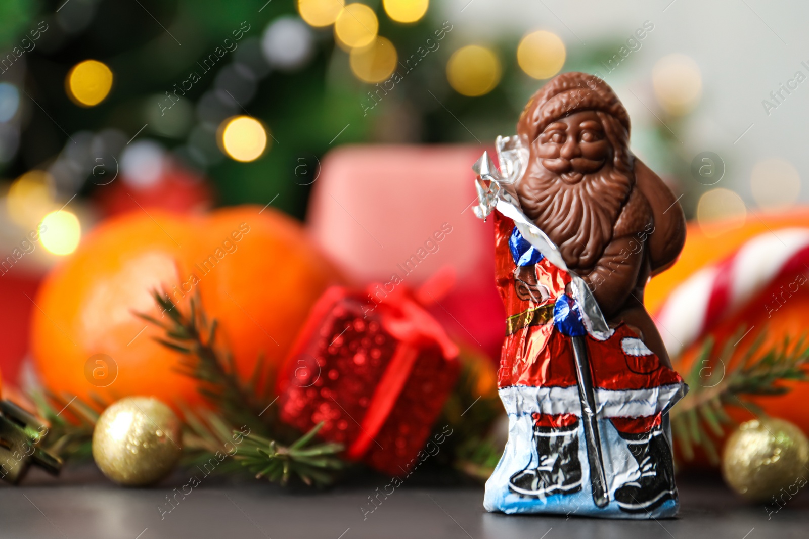 Photo of Chocolate Santa Claus candy against Christmas decorations, sweets and tangerine fruits, space for text