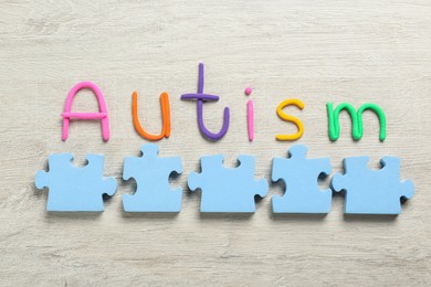 Photo of Flat lay composition with jigsaw puzzle pieces and word Autism on wooden background