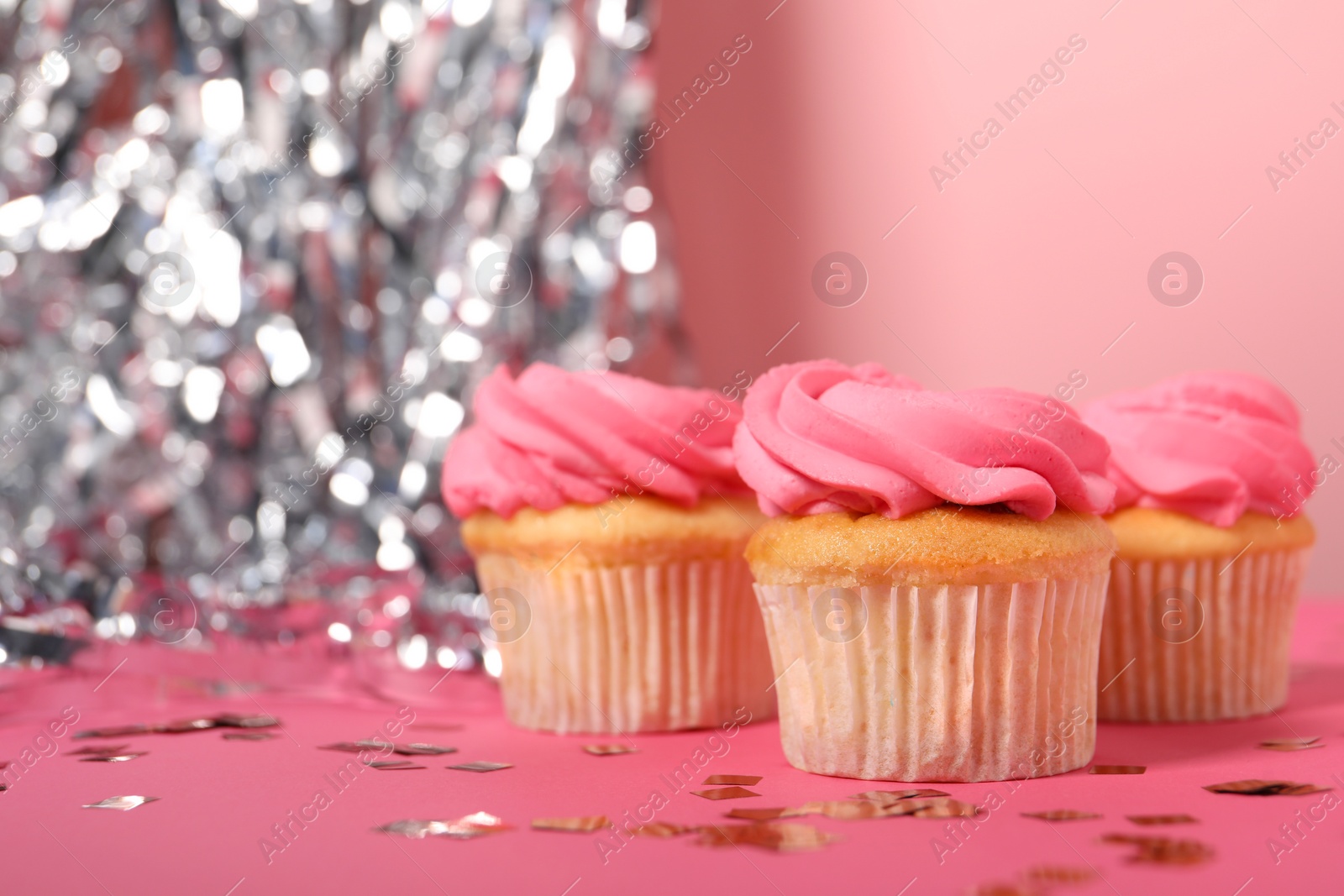 Photo of Delicious cupcakes with bright cream and confetti on pink background