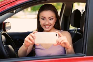 Beautiful young woman taking selfie in car