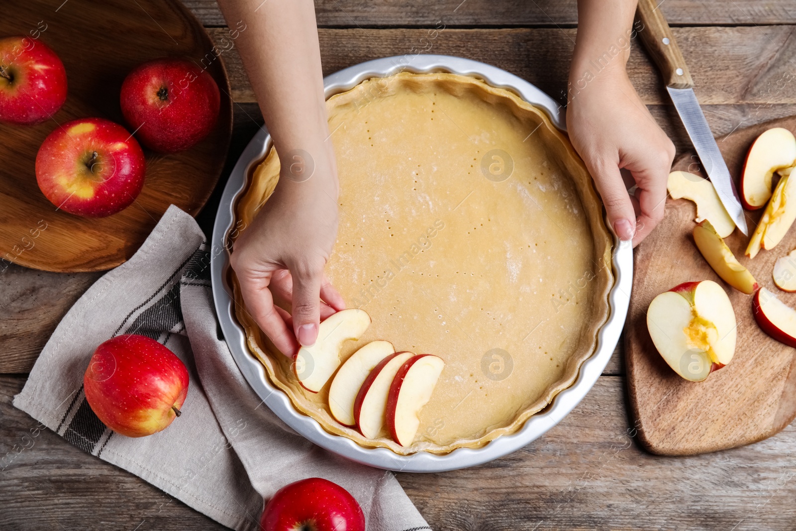 Photo of Woman putting apple slice into baking dish with dough to make traditional English pie at wooden table, top view