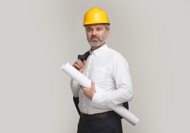 Architect in hard hat holding draft on grey background