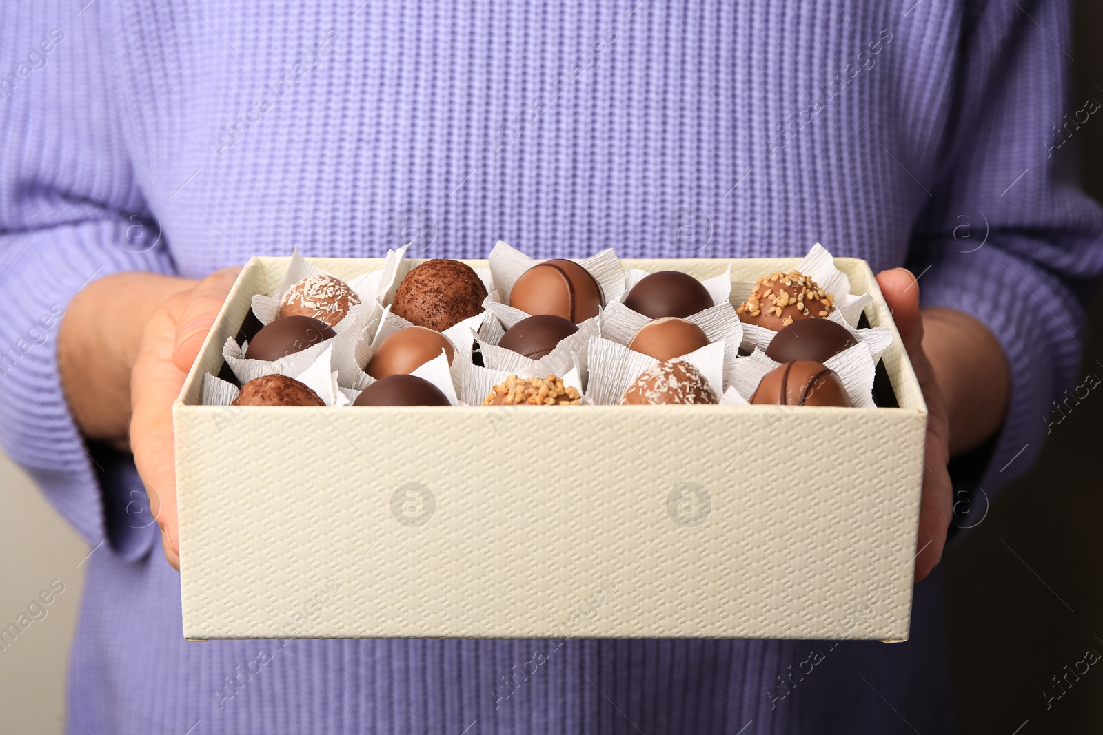 Photo of Woman holding box of delicious chocolate candies, closeup