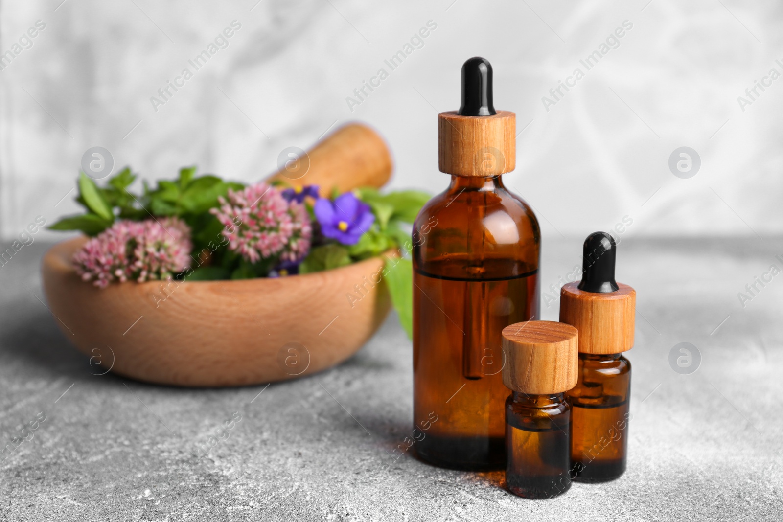 Photo of Glass bottles of essential oil and mortar with different wildflowers on light grey table, closeup
