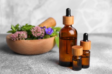 Photo of Glass bottles of essential oil and mortar with different wildflowers on light grey table, closeup