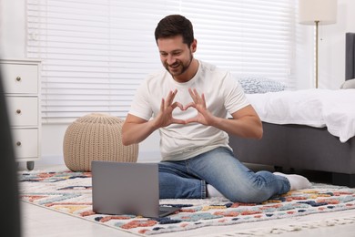 Photo of Happy man making heart with hands during video chat via laptop at home. Long-distance relationship