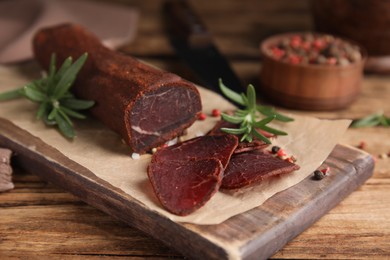 Photo of Delicious dry-cured beef basturma with rosemary and peppercorns on wooden table, closeup