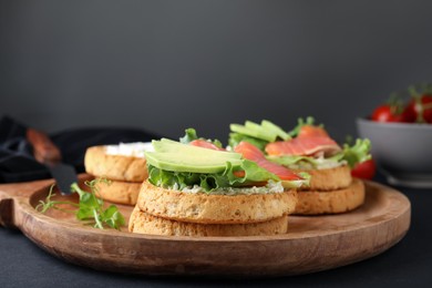 Photo of Tasty rusks with salmon, cream cheese and avocado served on black table, closeup