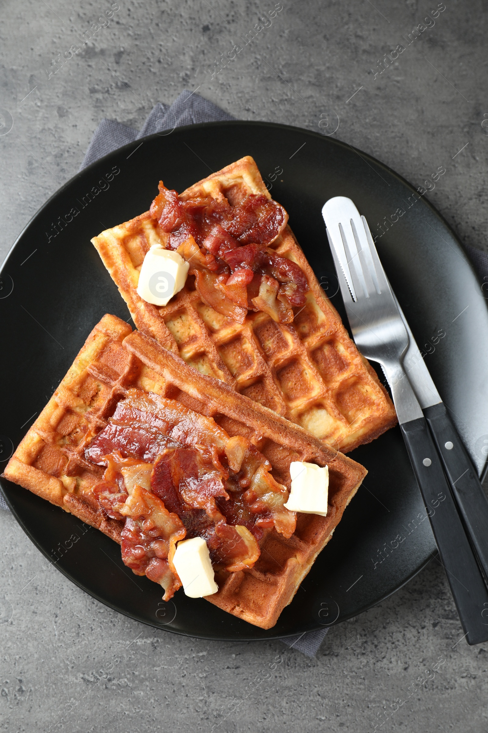 Photo of Tasty Belgian waffles served with bacon and butter on grey table, top view