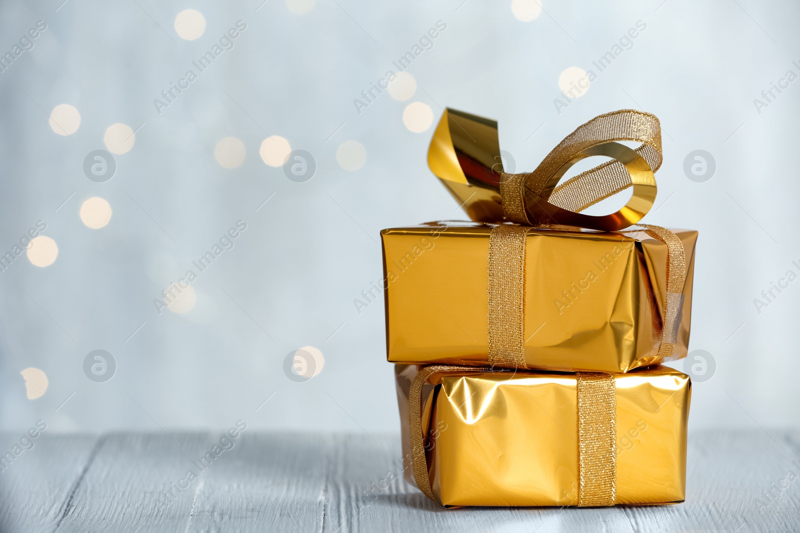 Photo of Golden gift boxes on white table against blurred lights, space for text