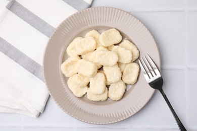 Photo of Plate of tasty lazy dumplings and fork on white tiled table, flat lay