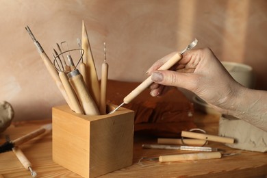 Photo of Woman taking clay crafting tool from wooden holder in workshop, closeup