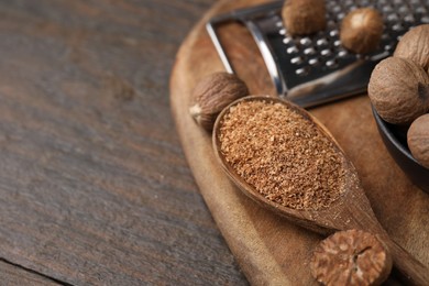Spoon with grated nutmeg, seeds and grater on wooden table, closeup. Space for text