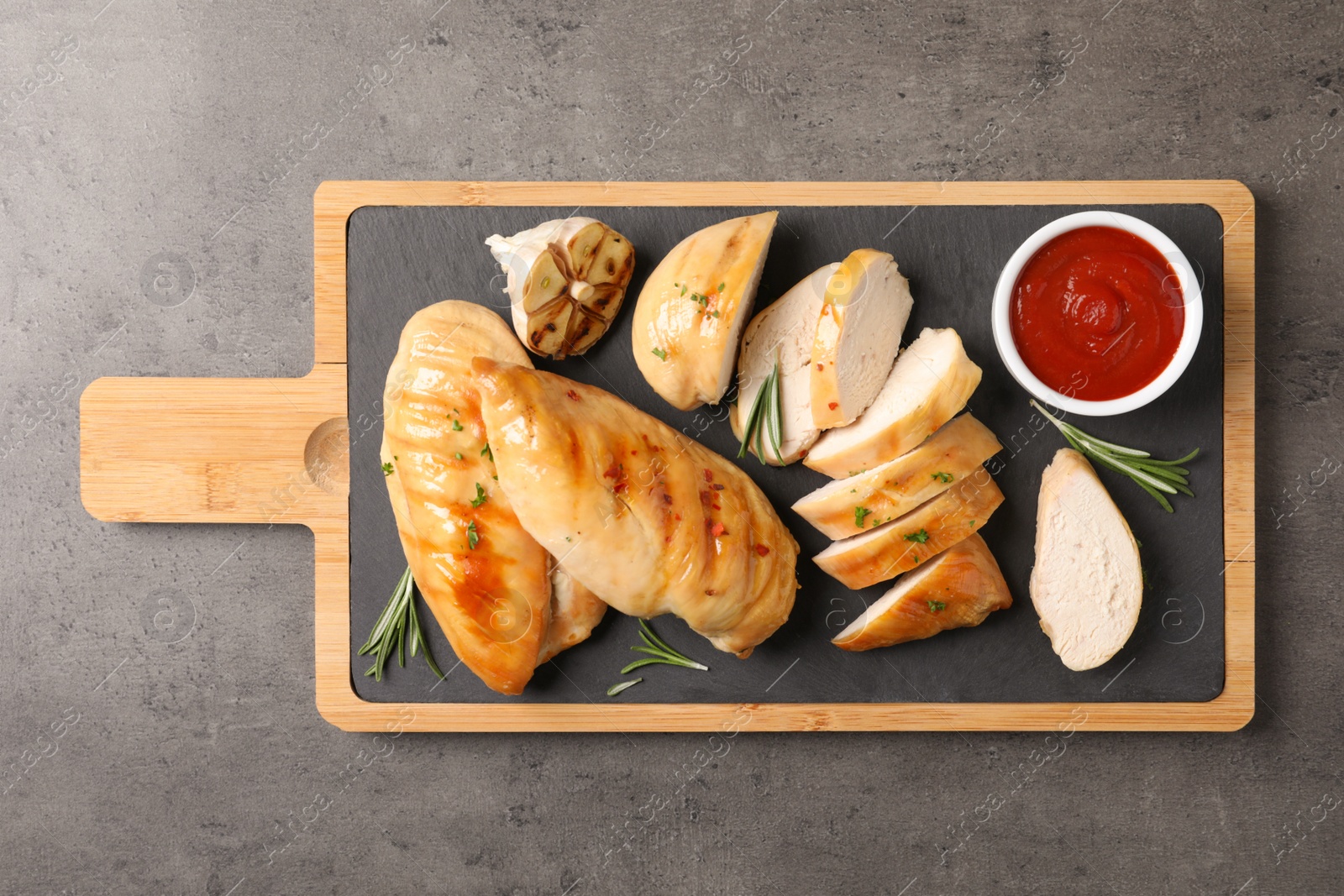 Photo of Board with fried chicken breasts and sauce on grey background, top view