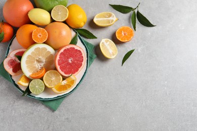 Different citrus fruits with fresh leaves on light grey table, flat lay. Space for text