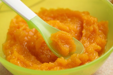 Baby food. Bowl with tasty pumpkin puree on beige textured table, closeup