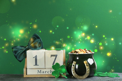 Image of Composition with pot of gold coins and wooden block calendar on grey stone table against green background. St. Patrick's Day celebration