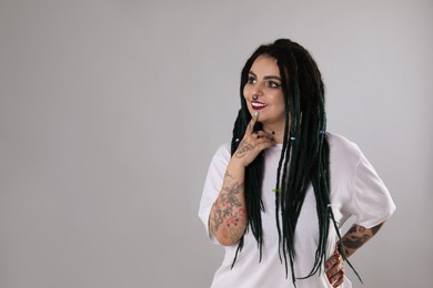 Beautiful young woman with tattoos on arms, nose piercing and dreadlocks against grey background. Space for text