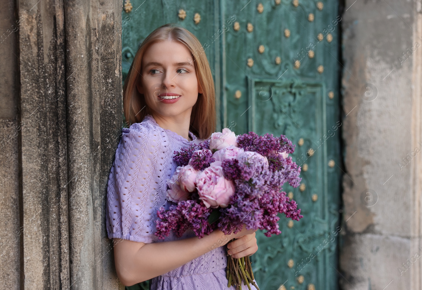 Photo of Beautiful woman with bouquet of spring flowers near building outdoors