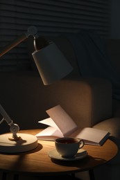 Photo of Stylish lamp, book and cup of tea on side table indoors