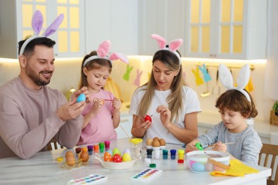 Easter celebration. Happy family with bunny ears painting eggs at white marble table in kitchen