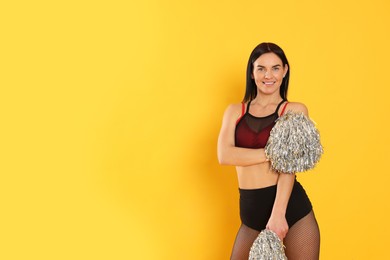 Photo of Beautiful cheerleader in costume holding pom poms on yellow background. Space for text