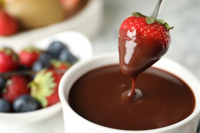 Photo of Dipping strawberry into fondue pot with chocolate, closeup