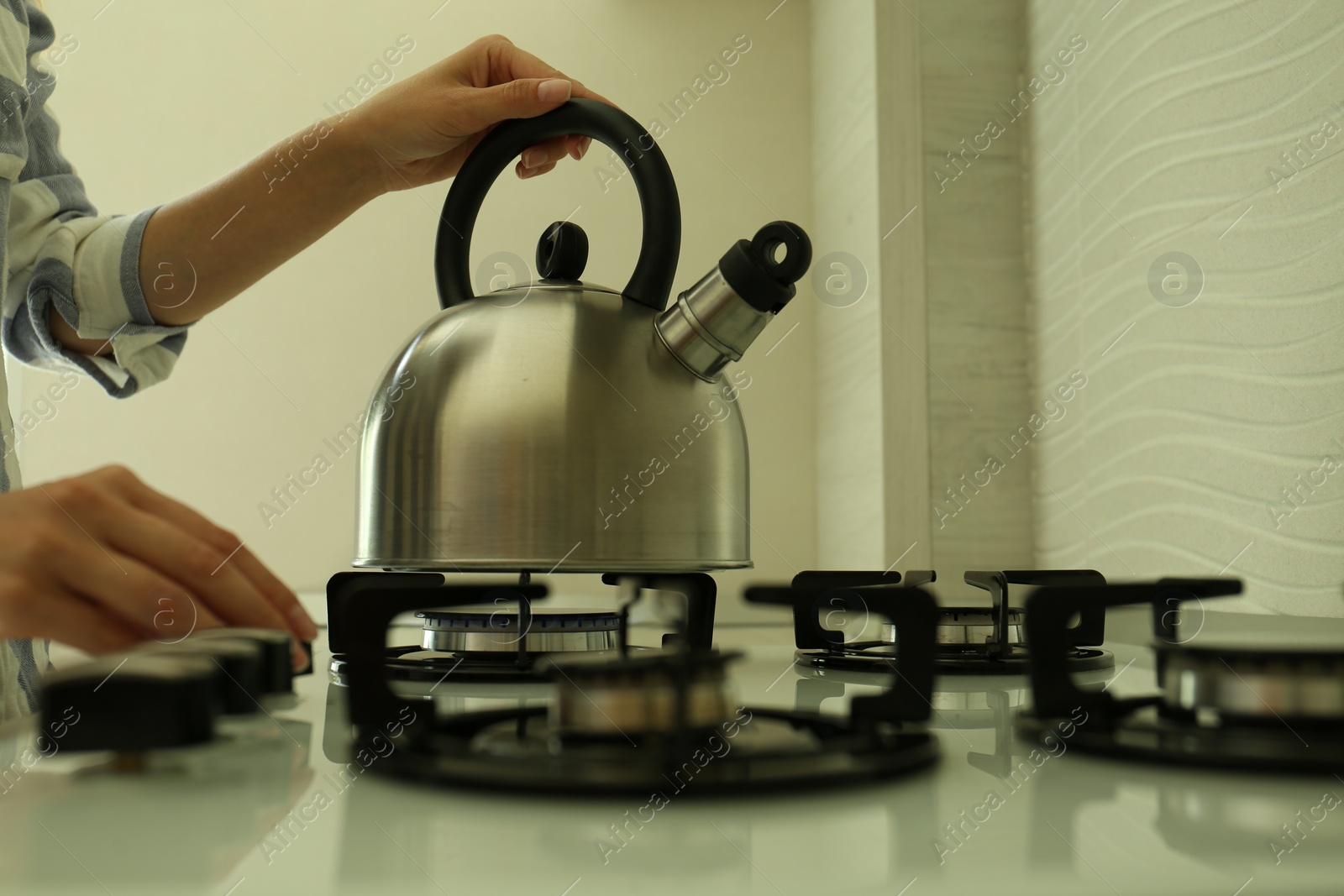 Photo of Woman putting kettle on gas stove in kitchen, closeup