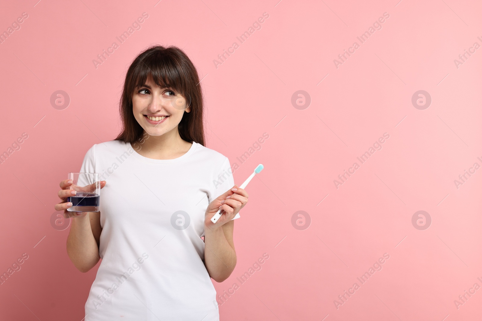 Photo of Young woman with mouthwash and toothbrush on pink background, space for text