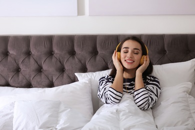Photo of Young woman with headphones enjoying music in bed