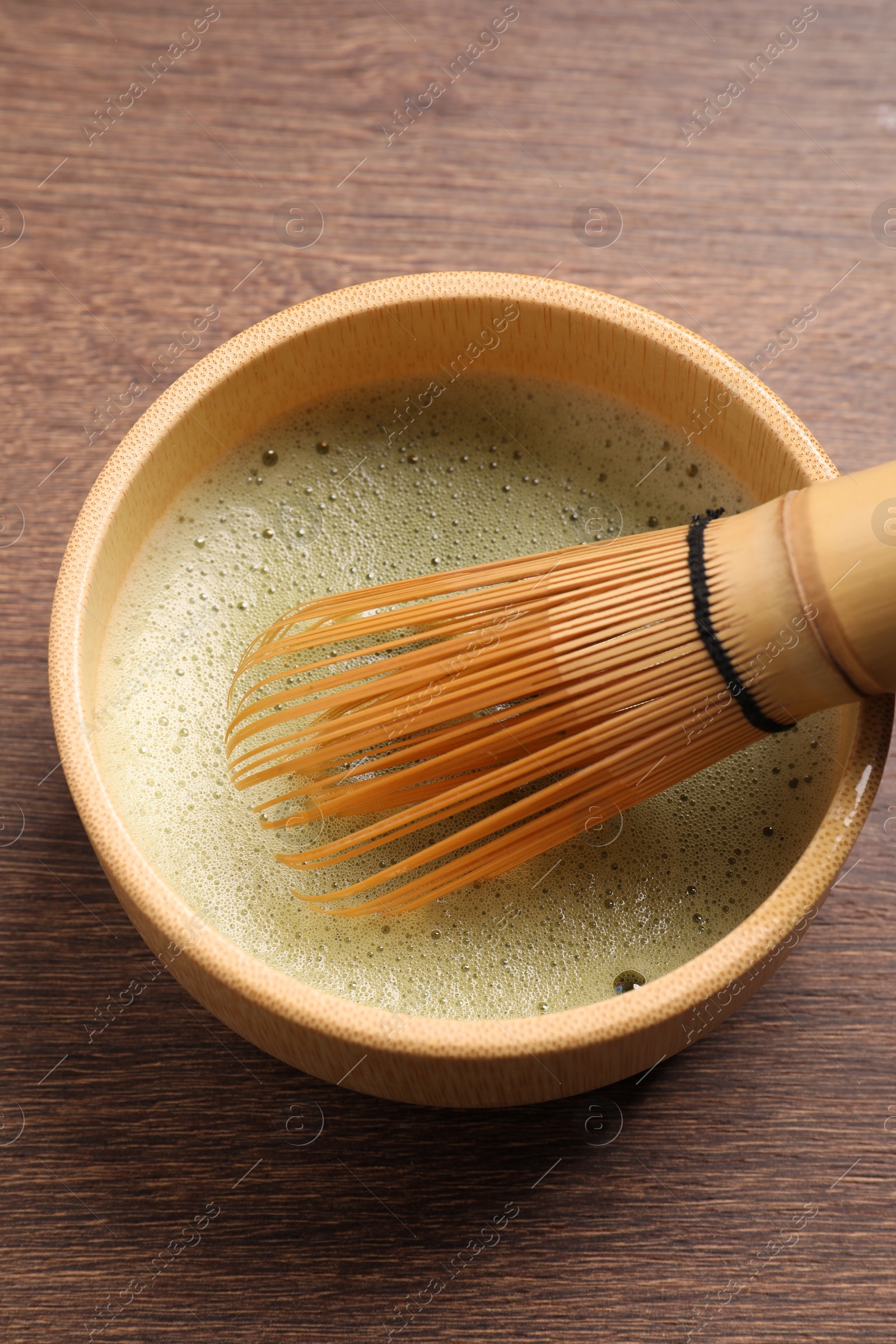 Photo of Cup of matcha tea and bamboo whisk on wooden table, above view