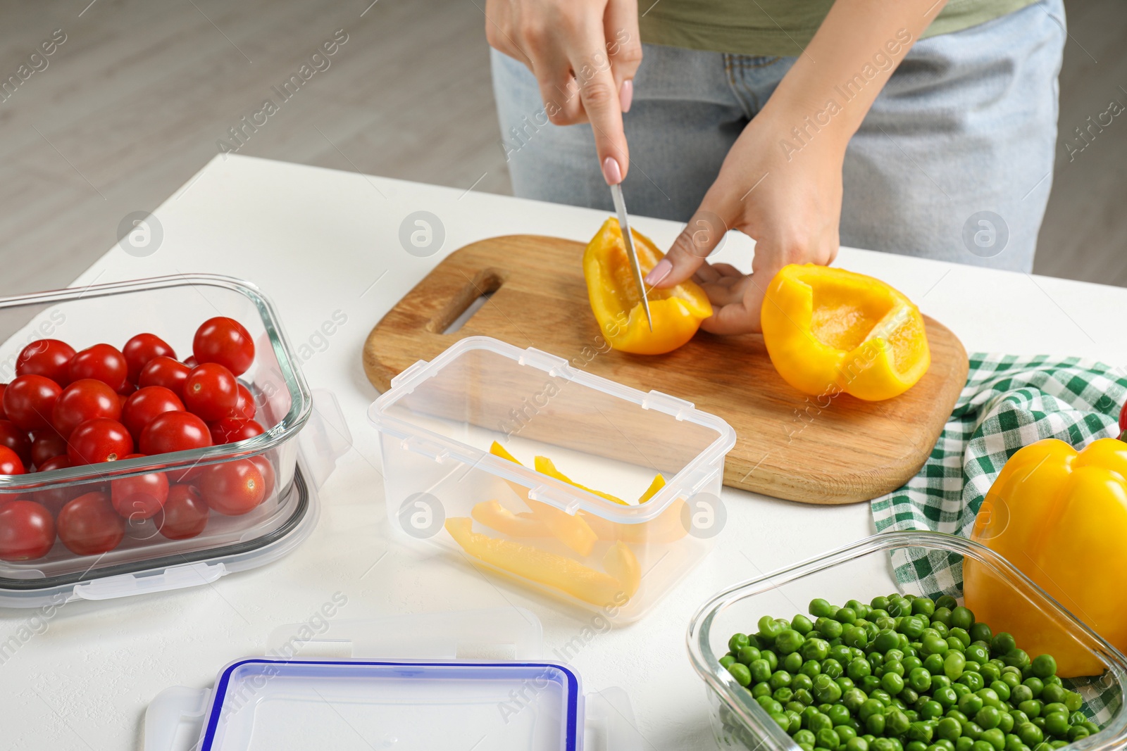 Photo of Woman cutting bell pepper and containers with fresh products on white table, closeup. Food storage