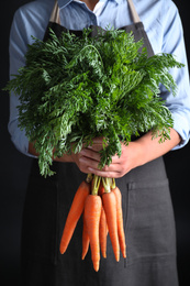 Photo of Woman holding ripe carrots on black background, closeup