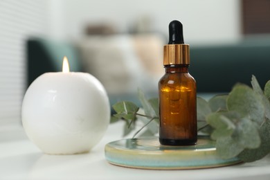 Photo of Aromatherapy. Bottle of essential oil, burning candle and eucalyptus leaves on white table