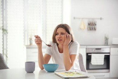 Photo of Sleepy young woman eating breakfast at home in morning